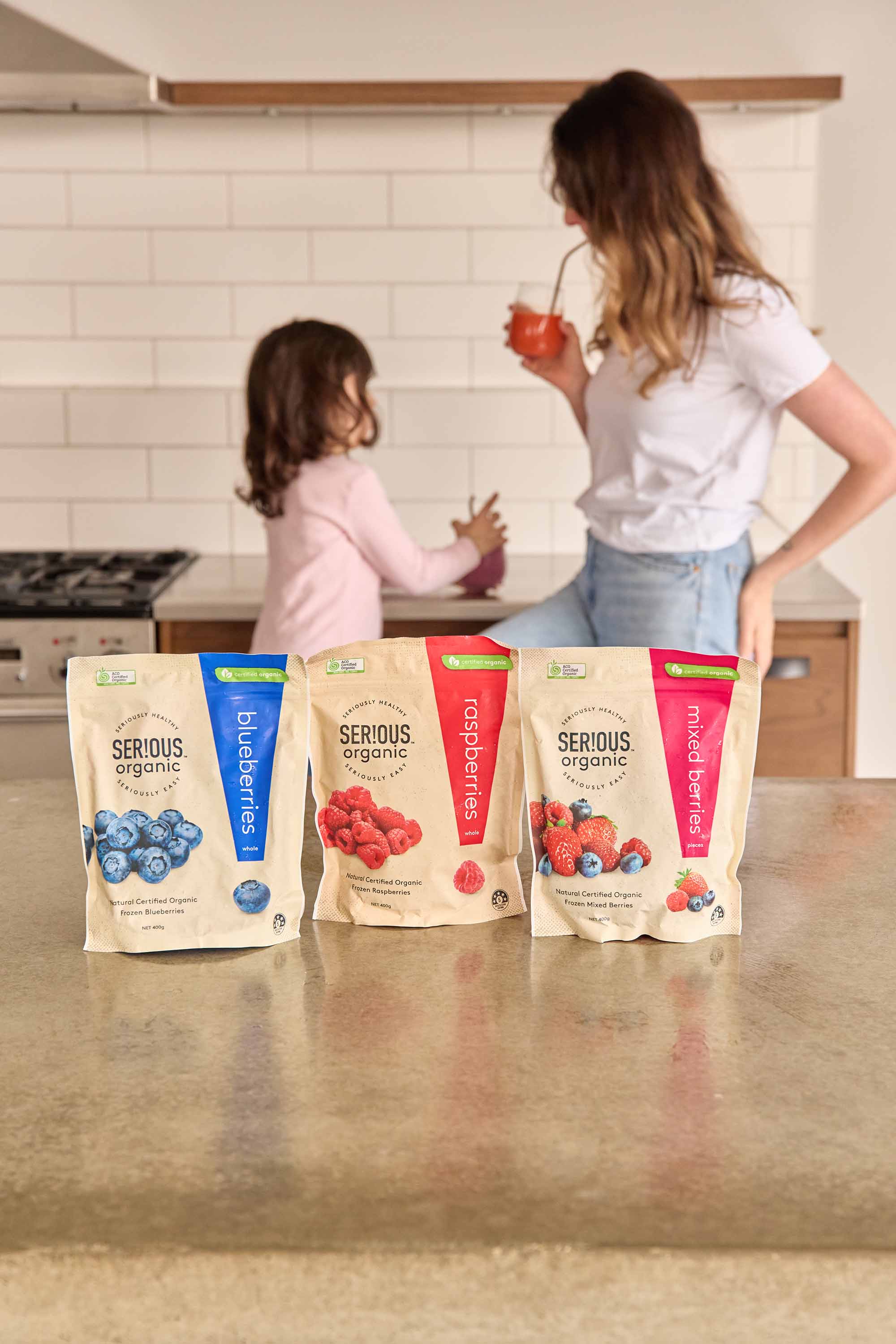 Mum and daughter in kitchen behind Serious Organic frozen fruit range on counter
